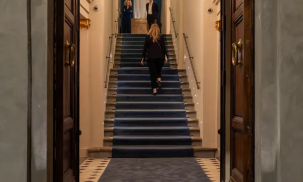Grand staircase and guest arrival at Teatro Nazionale Firenze Grand staircase lined with blue carpet seen through open wooden double doors with guests at Teatro Nazionale Firenze